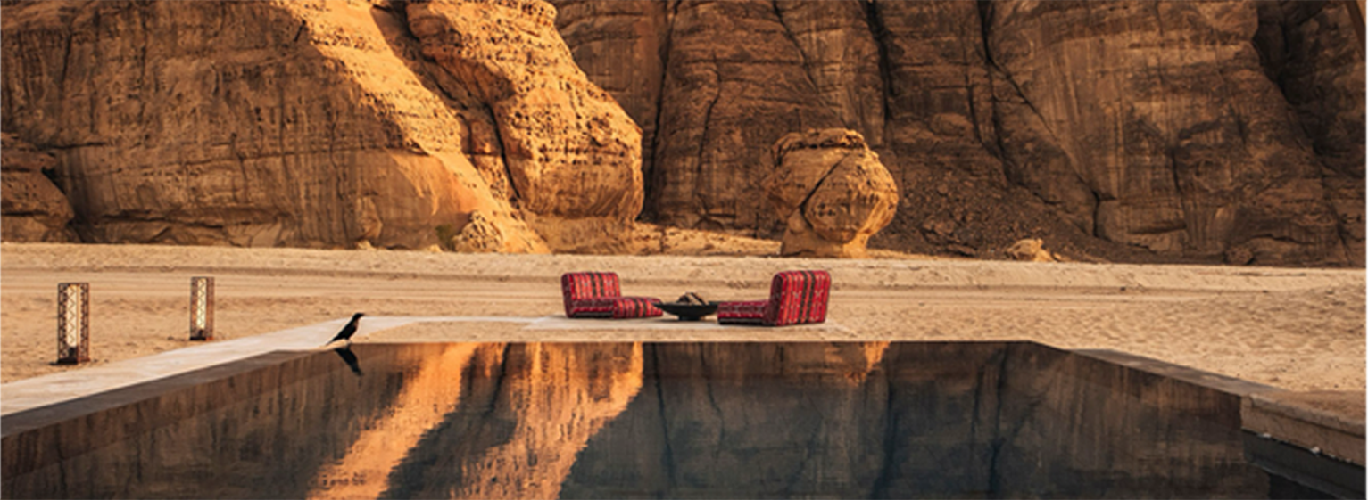 AlUla resort reflected in water between sandstone cliffs