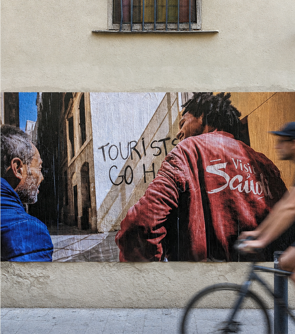 Street mural with a visitor in a blue jacket beside tourists go home graffiti